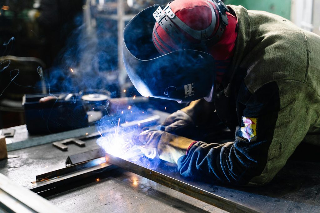 pexels-photo-2381463-2381463 A welder works on metal fabrication indoors, creating bright sparks and smoke.